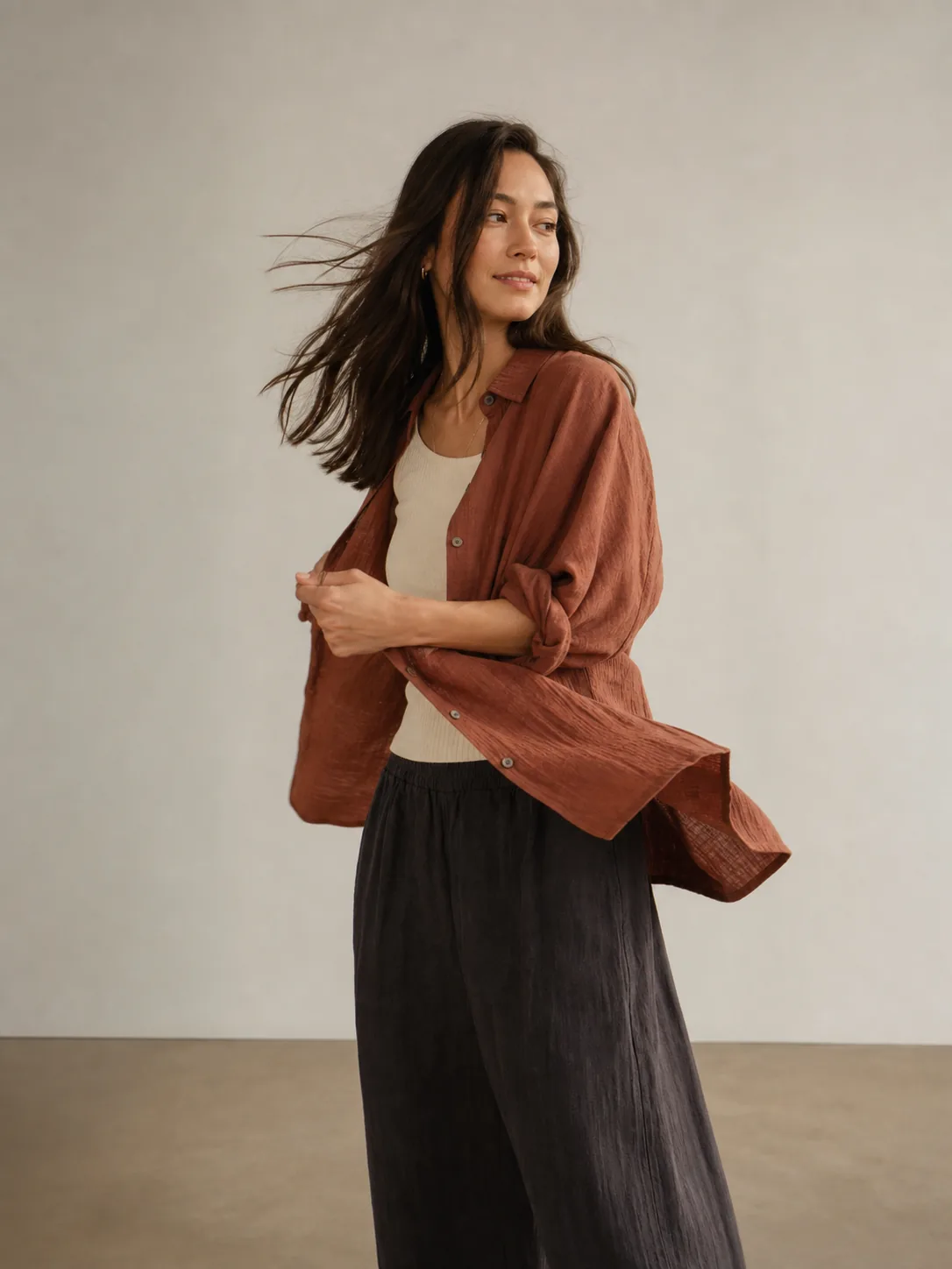 Person turning in a warm studio with her hair and rust-colored overshirt caught in motion